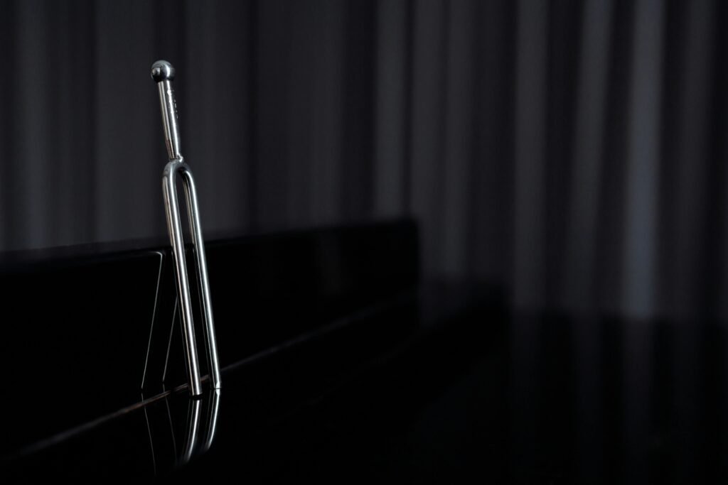 pexels-photo-6194031-6194031 A close-up of a metal tuning fork standing on a reflective piano surface with dark background.