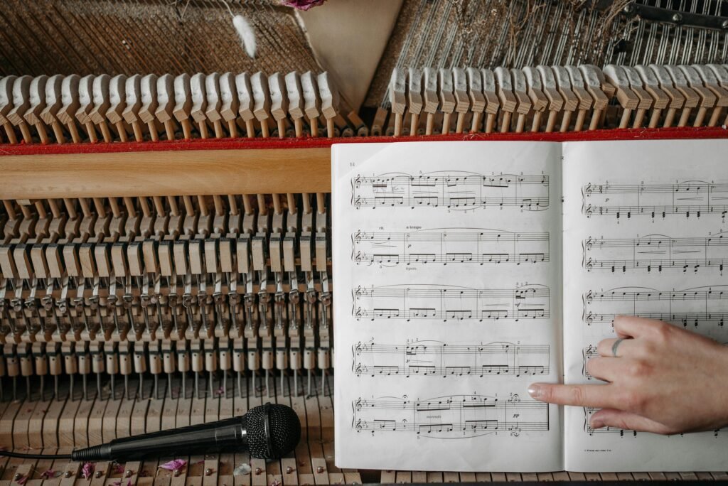 pexels-photo-7521175-7521175 Closeup of piano interior and sheet music with hand pointing, microphone nearby.