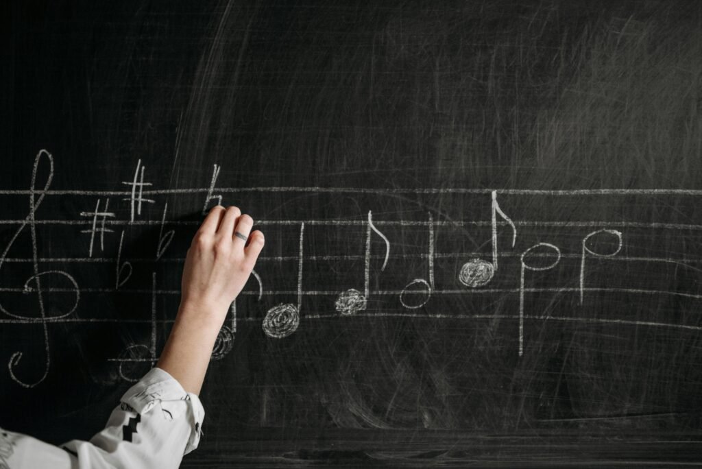 pexels-photo-7521300-7521300 A person writing musical notes on a blackboard with chalk indoors.